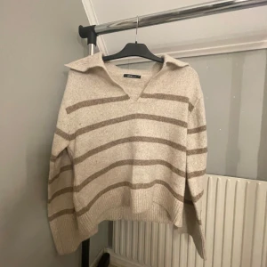 Beige och brun randig tröja från Gina  - Säljer en mysig beige tröja med bruna ränder från gina tricot. Tröjan har en v-ringad krage och långa ärmar. 
