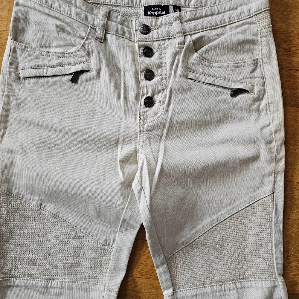 Snygga beige jeansbyxor från KappAhl med unika detaljer. Byxorna har knappar framtill och förstärkta knän med textur. Kedjan på benen nertill på sidan. Midjehöjd ( lågmidjade) 23,5 innerbensmått 74 cm Midjan 39*2. Farkut & Housut.