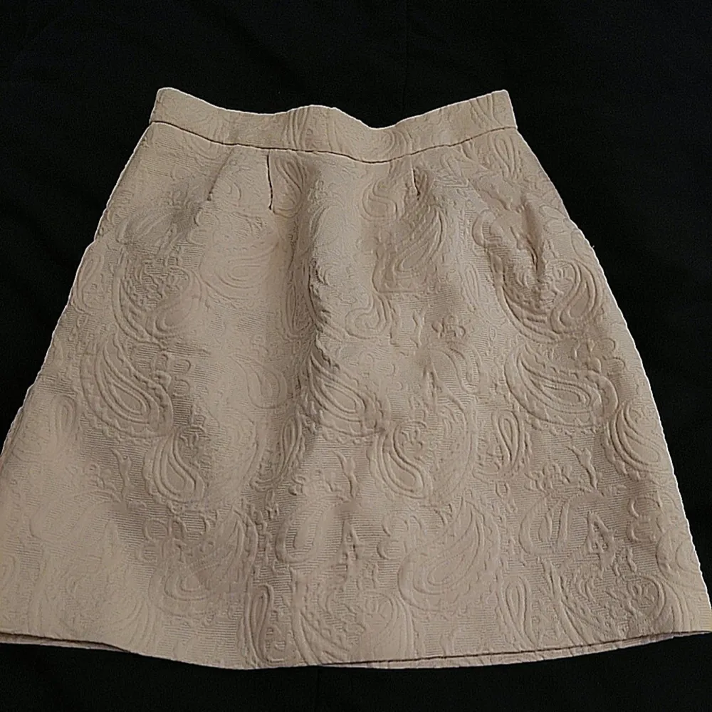 Snygg beige kjol från H&M med ett subtilt mönster i tyget. Kjolen har en klassisk A-linjeform och är perfekt för en stilren look. Den är i storlek 34 och passar perfekt för dig som gillar en elegant stil.. Hameet.