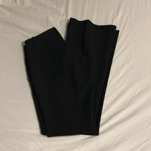 Lågmidjade kostymbyxor  - Snygga svarta kostymbyxor från Mango med låg midja och bootcut-stil. Perfekta för en stilren look. Byxorna har en klassisk design med hällor för bälte och diskreta fickor.