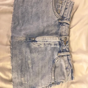 Ljusblå jeanskjol från Zara - Säljer en snygg ljusblå miniskirt från Zara. Kjolen har en rå kant nertill för en trendig look. Perfekt för varma dagar och kan matchas med olika toppar för en avslappnad stil. Väldigt kort men extremt fin på.