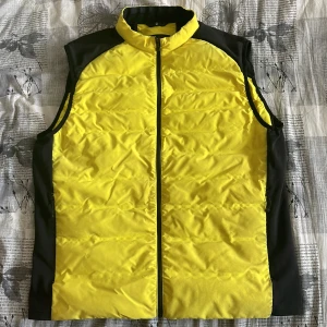 Gul och svart väst från SAIL RACING - Snygg gul och svart väst med dragkedja framtill. Perfekt för en sportig look eller som ett extra lager under kyliga dagar. Västen har en modern design med kontrasterande svarta paneler på sidorna.