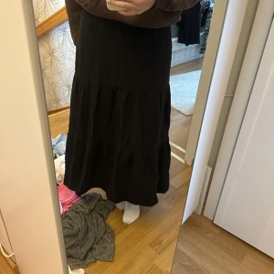 Svart långkjol - Säljer en stilren svart långkjol med volangdetaljer. Kjolen har en avslappnad passform och är perfekt för olika tillfällen. Den är enkel att matcha med olika toppar och accessoarer.