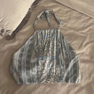 Mönstrad halterneck topp - Säljer en snygg halterneck topp med mönster i blått och vitt. Toppen har knytband i nacken och en öppen rygg. Perfekt för sommardagar