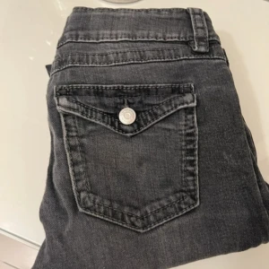 Grå jeans från Gina Tricot - Snygga grå jeans från Gina Tricot med klassisk femficksdesign och knappdetaljer. Perfekta för en avslappnad stil med en modern touch. Passar bra till olika outfits och tillfällen.