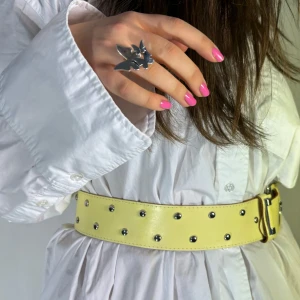 Gult bälte med nitar - Snyggt gult bälte med silverfärgade nitar och ett matchande spänne. Perfekt för att ge din outfit en cool touch. Bältet är brett och passar bra till både klänningar och byxor. 💞88 cm