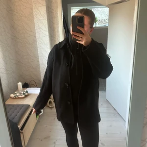 Svart kappa med knappar - Snygg svart kappa med knappar framtill. Perfekt för kyligare dagar med sin klassiska design och långa ärmar. En stilren och tidlös jacka som passar till många tillfällen. Ifrån arket 
