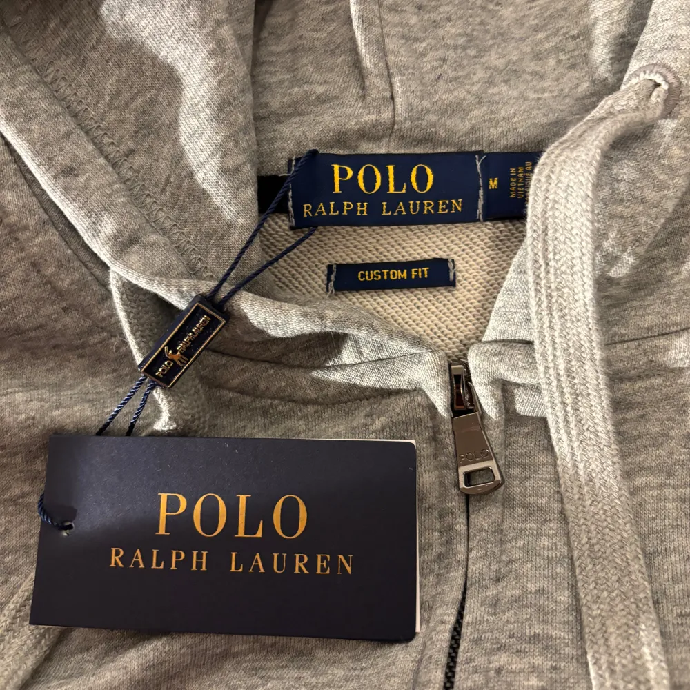 Säljer en snygg grå hoodie från Polo Ralph Lauren i storlek M. Den är i nytt skick med etikett kvar. Hoodien har dragkedja och en broderad logga på bröstet. Perfekt för både höst och vår!. Tröjor & Koftor.