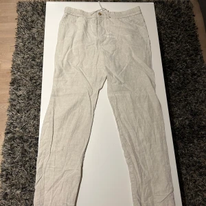 Beige linnebyxor Skagen storlek L, passar till M - Snygga beige linnebyxor med en avslappnad passform. De har en knapp framtill och är perfekta för varma dagar. Byxorna är tillverkade i ett lätt och luftigt material som ger en skön känsla.