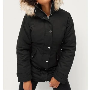 Svart parkajacka med päls - Säljer en snygg svart parkajacka med fuskpäls på huvan. Jackan har långa ärmar och stängs med både dragkedja och knappar. Perfekt för kalla vinterdagar och höstpromenader. Den är i mycket bra skick och supermysig att ha på sig! Som en XXL 