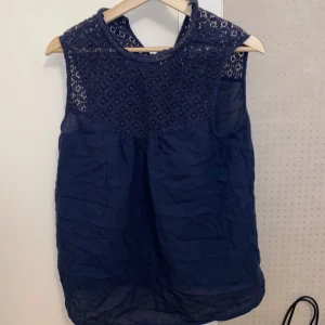 Mörkblå ärmlös blus med spetsdetaljer - Snygg mörkblå blus från Kappahl med spetsdetaljer upptill. Blusen är ärmlös och har en rund halsringning. 