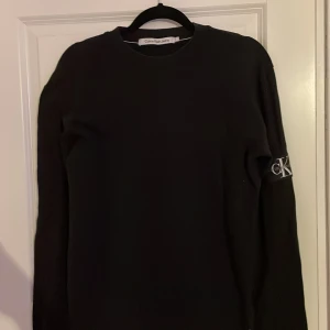 Svart tröja från Calvin Klein Jeans - Snygg svart tröja från Calvin Klein Jeans med långärmad design. Tröjan har en stilren look med CK-logga på ärmen. Perfekt för en casual och trendig stil. Storlek S