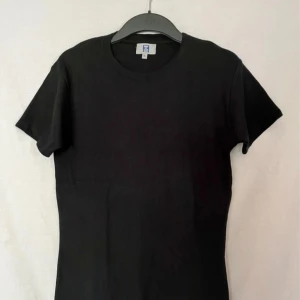 Svart t-shirt från Hallmans - Säljer en klassisk svart t-shirt från Hallmans i 100% bomull. Perfekt basplagg för alla tillfällen! Den är kortärmad och har en normal passform. Superbekväm och lätt att matcha med allt i garderoben. Tvättas enkelt i 40 grader.