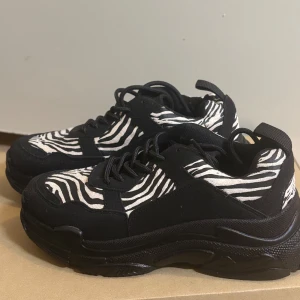 Svarta sneakers med zebramönster - Snygga svarta sneakers med zebramönster i vitt och svart. Skorna har en chunky sula och snörning framtill, vilket ger dem en trendig look.