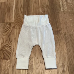 Vita babybyxor med pandamotiv från Mywearbaby - Söta vita babybyxor från Mywearbaby med ett gulligt pandamotiv på baksidan. Byxorna har breda muddar vid midja och benslut för extra komfort. Perfekta för de minsta!