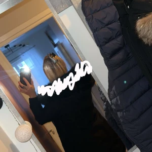 Svart parkajacka med pälsdetaljer - Snygg svart parkajacka med pälsdetaljer på huvan. Jackan har dragkedja och knappar framtill samt praktiska fickor. Perfekt för kyliga dagar. Finns även päls för armarna samt 2 st vid dragkedjan som man får med.