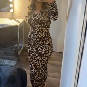 Leopardmönstrad långklänning - Trendig leopardmönstrad långklänning med långärmad design. Perfekt för att sticka ut med stil. Klänningen har en tight passform som framhäver figuren.