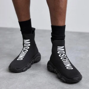  Moschino skor - Snygga svarta sneakers från Moschino med en unik design och tydlig logotyp på ovansidan. Skorna har en strumpliknande passform och en robust sula som ger bra stöd. Perfekta för en trendig och bekväm stil. Dessa skor är i storlek 44 och är äkta såklart.