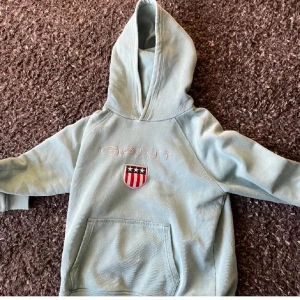 Grå hoodie från GANT - Säljer en snygg grå hoodie från GANT med en cool logga på bröstet. Den har en stor ficka fram och en bekväm huva. Perfekt för en avslappnad stil eller kyliga dagar. Passar både till vardags och chillkvällar. 🧢