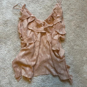 Rosa Zara linne med volanger - Säljer en superfin rosa linnetopp från Zara med blommigt mönster och volanger framtill. Toppen är ärmlös med smala axelband och har en luftig passform, perfekt för sommardagar eller en festlig kväll. Passar både till jeans och kjol!