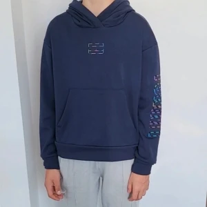 Tommy Hilfiger 146/152 - Säljer ett par grå mjukisbyxor med tryck på benet. Byxorna har en bakficka och elastisk midja för extra komfort. Perfekta för en avslappnad stil.