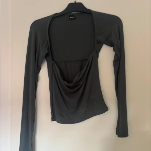 Grön långärmad topp från Gina Tricot - Snygg grön långärmad topp från Gina Tricot med en unik draperad design framtill. Toppen har en åtsittande passform och är perfekt för en stilren look.