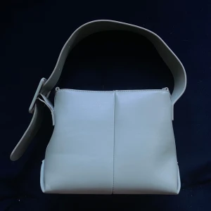 Grön axelväska med justerbart spänne - Elegant grön axelväska i syntetmaterial med ett brett justerbart spänne. Väskan har en praktisk dragkedja upptill och flera fack inuti för enkel organisering. Perfekt för en stilren look. Nest sista bilen beskriver motsvarar färgen bäst!