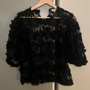 Svart blus från Object - Snygg svart blus från Object i storlek 40. Den har ett genomskinligt tyg med blommigt mönster och trekvartsärmar. Perfekt för en festlig kväll eller en utekväll med vänner. Blusen är både elegant och trendig!