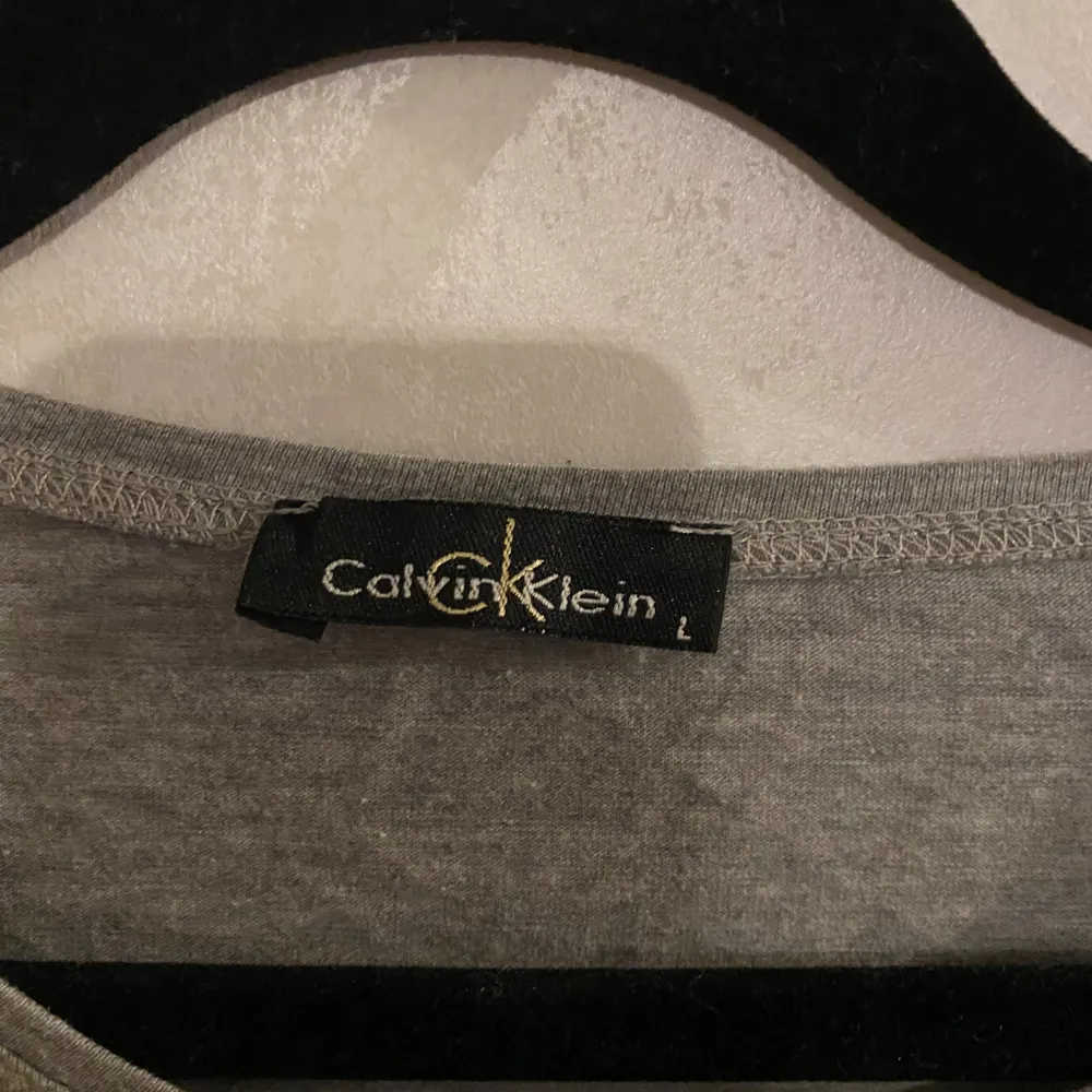 Säljer en snygg grå t-shirt från Calvin Klein i storlek L. Den har en stor logga på framsidan och är gjord i mjukt bomullsmaterial. Perfekt för en avslappnad stil eller vardagsbruk. Kortärmad och i bra skick!. T-paidat.