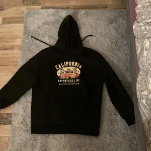 Säljer en svart hoodie med coolt tryck av en vintage bil och texten 'California Adventure Life'. Perfekt för en avslappnad stil. Den har en stor huva och långa ärmar, vilket gör den perfekt för kyligare dagar. Passar bra till jeans eller joggers! Den är markerad S men skulle passa M också, då den är lite oversize!