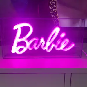 neonskylt med texten 'Barbie' i rosa. Perfekt för att liva upp rummet. Skylten är innesluten i en transparent låda och drivs med USB-anslutning. Säljer för den inte kommit till användning. Kan mötas upp för säljning runt om i Kungsbacka.💕