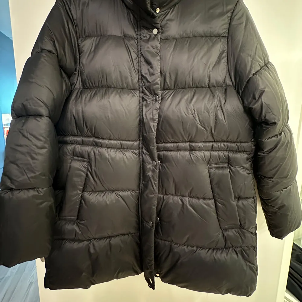 Säljer en svart mango dunjacka med hög krage och knäppning framtill. Jackan har en quiltad design och långa ärmar, perfekt för kalla dagar. Den har både dragkedja och knappar för extra skydd mot kyla. Str m men passar en s också använd ett par gånger men i fin skick . Takit.