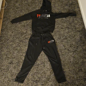 Svarta mjukisbyxor från Trapstar - Säljer ett par svarta mjukisbyxor från Trapstar med snörning i midjan och logotyp i vitt och rött på benet. Perfekta för en avslappnad stil.den är helt nytt. Storlek är s.pris diskutera. +46765808518