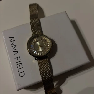 Guldfärgad klocka från Anna Field - Snygg guldfärgad klocka från Anna Field med ett glittrigt urtavla. Klockan har en stilren design med en rund urtavla och guldfärgade visare. Använts mycket men inga defekter och den funkar som den ska. Klockan säljes med förpackning. 