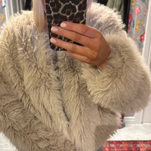 Beige teddyjacka - Supermysig beige teddyjacka i fluffigt material. Perfekt för att hålla sig varm och stilren under kyliga dagar. Jackan har en normal passform och långa ärmar, vilket gör den idealisk för både höst och vinter. Ett måste för garderoben om du älskar att mysa till det!