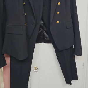 Svart kavaj med guldknappar och byxa - Elegant svart kavaj med stiliga guldknappar. Perfekt för formella tillfällen. Kavajen har en klassisk design med fickor och en snygg passform.