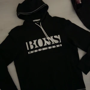 Svart hoodie från Hugo Boss (slutsåld överallt i alla storlekar!) - Säljer en svart hoodie från Hugo Boss med vit logga på bröstet. Använts max 2 gånger innan. Nypris på asos för 1759kr. Jag säljer för mycket billigt pris. 