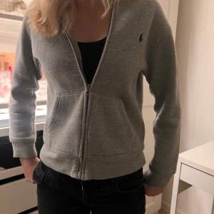 Grå hoodie med dragkedja - Säljer en snygg och bekväm grå hoodie från Polo Ralph Lauren. Den har en dragkedja framtill och en liten logga på bröstet. Perfekt för en avslappnad stil och passar till alla tillfällen. 🐴