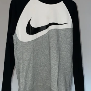 Grå och svart Nike dress - Säljer en snygg och bekväm tröja från Nike med tillhörande byxor i grått och svart. Den har ett stort Nike-logotyptryck på framsidan och långa svarta ärmar. Perfekt för träning eller en avslappnad dag. Passar bra till alldaglig användning året om.  Storlek M, byxor och tröja  passar även S 