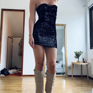 Svart paljettklänning nyår fest klänning - Snygg svart axelbandslös klänning med paljetter som glittrar i ljuset. Perfekt för fest eller nyår!❤️‍🔥❤️‍🔥 Den är tight och kort, vilket ger en elegant och festlig look. Klänningen har en smickrande passform och är i mycket bra skick!🐆🐆