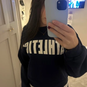 Mörkblå sweatshirt med text - Säljer en mörkblå sweatshirt med vit text 'ATHLETIC' på framsidan. Tröjan har en avslappnad passform och långa ärmar, perfekt för en chill dag eller träning. Superbekväm och stilren! ( från Young Gina och är i stolek 158/164 ) 