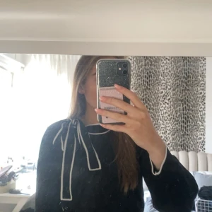 Svart tröja med vit knytrosett - Säljer en elegant svart tröja med en vit knytrosett vid halsen. Tröjan har långa ärmar och vita detaljer längs kanterna. Perfekt för både vardag och fest! 🖤 aldrig använd bara testad, men tog bort lappen så kan ej lämna tillbaka!