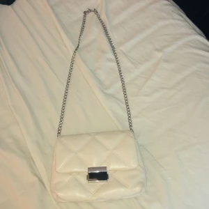 Vit quiltad axelväska med kedja - Säljer en superfin vit quiltad axelväska med en elegant kedja. Väskan har en stilren design med ett metallspänne framtill. Perfekt för både vardag och fest! 👜✨