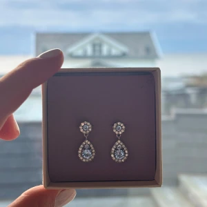 Glittriga örhängen med blå stenar - Eleganta örhängen med droppformade blå stenar omgivna av gnistrande kristaller.