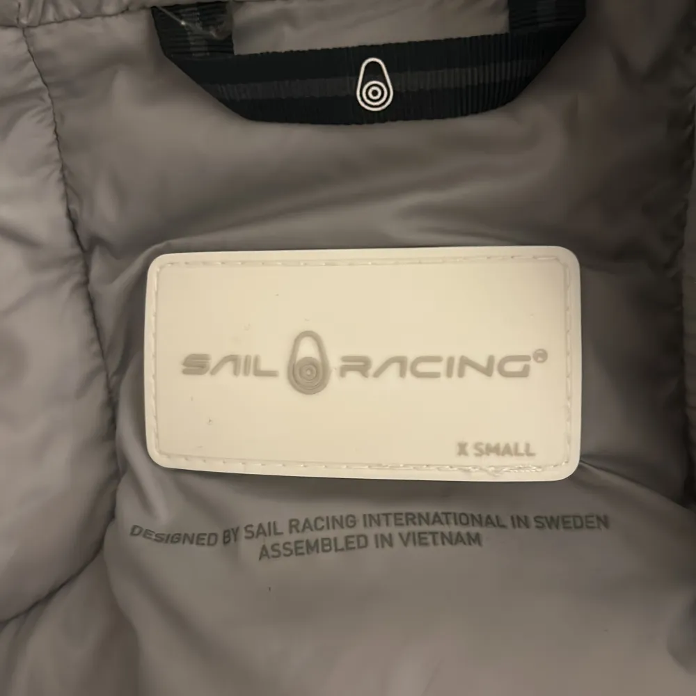 Säljer en grön dunjacka från Sail Racing i storlek XS. Jackan har en hög krage och huva för extra värme. Den är utrustad med dragkedja och har en stilren design. Perfekt för kyliga dagar.. Takit.