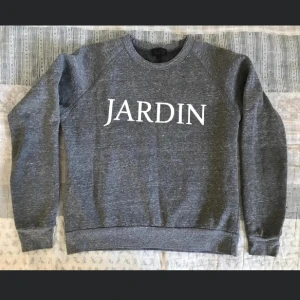 Grå sweatshirt med texten JARDIN - Säljer en stilren grå sweatshirt med vit text 'JARDIN' på bröstet. Tröjan har en klassisk rund hals och långa ärmar. Perfekt för en avslappnad stil.