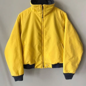 Gul jacka från Woolrich - Säljer en cool gul jacka från Woolrich med dragkedja och grå fleecefoder. Jackan har långa ärmar och ribbade muddar i svart vid ärmslut och nederkant. Perfekt för att lysa upp din stil!