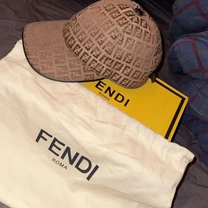 Beige keps från Fendi - Snygg beige keps från Fendi med ett ikoniskt mönster. Kepsen har en klassisk design med böjd skärm och justerbar passform. Perfekt för att ge en lyxig touch till din outfit.