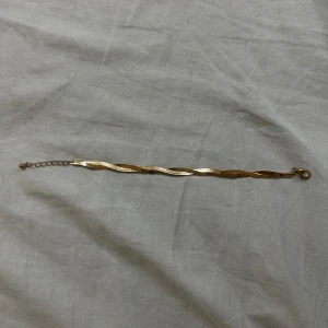 Guldarmband med vriden design - Elegant guldarmband med en vriden design som ger en unik och stilren look. Perfekt för att lägga till en touch av glamour till din outfit. Armbandet har en justerbar kedja för att passa olika storlekar.