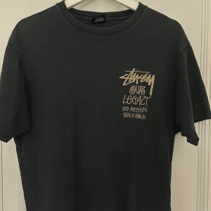 T-shirt, Stussy x Our Legacy - Säljer en grå/svart t-shirt från Stussy x Our Legacy. Tröjan är använd men okej skick. Storlek S men är stor i storlek. Made in USA. 